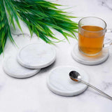 Set of marble coasters with a glass of tea and spoon on a marble surface with green leaves.