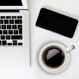 Laptop, smartphone, and coffee cup on a white surface