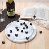 Marble coaster with black balls, bottle of Heaven sparkling wine, and open book on wooden surface