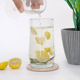 Person pouring liquid into a glass with lemon slices and mint leaves on a white surface.