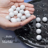 White marble balls held in a hand with a marble surface below.
