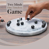 Two hands playing with marbles on a marble board, with text 'Two Minds One Timeless Game' above.