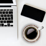 Laptop, smartphone, and coffee cup on a white surface