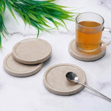 Set of stone coasters with a glass of tea and spoon on a marble surface.