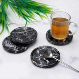Black marble coasters on a white surface with a glass of tea and spoon.