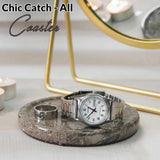 Silver watch on a marble coaster with candles and a mirror in the background
