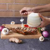 Person seasoning pizza with a salt shaker on a wooden board with ingredients.