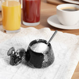 Black stone salt cellar with a spoon on a table with drinks in the background