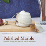 Polished marble salt cellar with spoon on a wooden cutting board