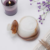 Decorative stone container with agate lid next to a lit purple candle and lavender flowers on a white surface.