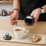 Person preparing a cup of coffee with cookies and a small container on a kitchen counter.