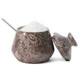 Decorative marble container with lid and spoon on a white background