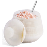 A  salt and pepper container with its lid leaning against the base, filled with pink Himalayan salt and topped with a metal spoon, on a white background.