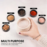 A hand holds a salt jar filled with coarse pink salt, surrounded by small black bowls labeled Pepper, Spices, Pink Salt, Almonds, and Sugar on a white surface. Text at the bottom reads 'MULTI PURPOSE'.