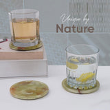 Glass with lemon slices on a marble coaster, next to another coaster and glass with a drink.