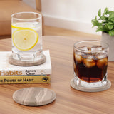 Glass with lemon slices on a marble coaster, next to another coaster and glass with a drink.