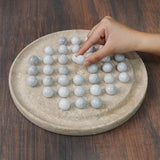 Hand interacting with marble-like balls on a stone tabletop game on a wooden surface