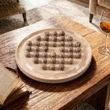 A marble  board holding 36 small round stone-like pieces, styled on a rustic wooden table with an open book and a wine glass in a warm indoor setting.