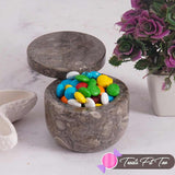 Marble container with colorful stones on a light surface with a plant in the background